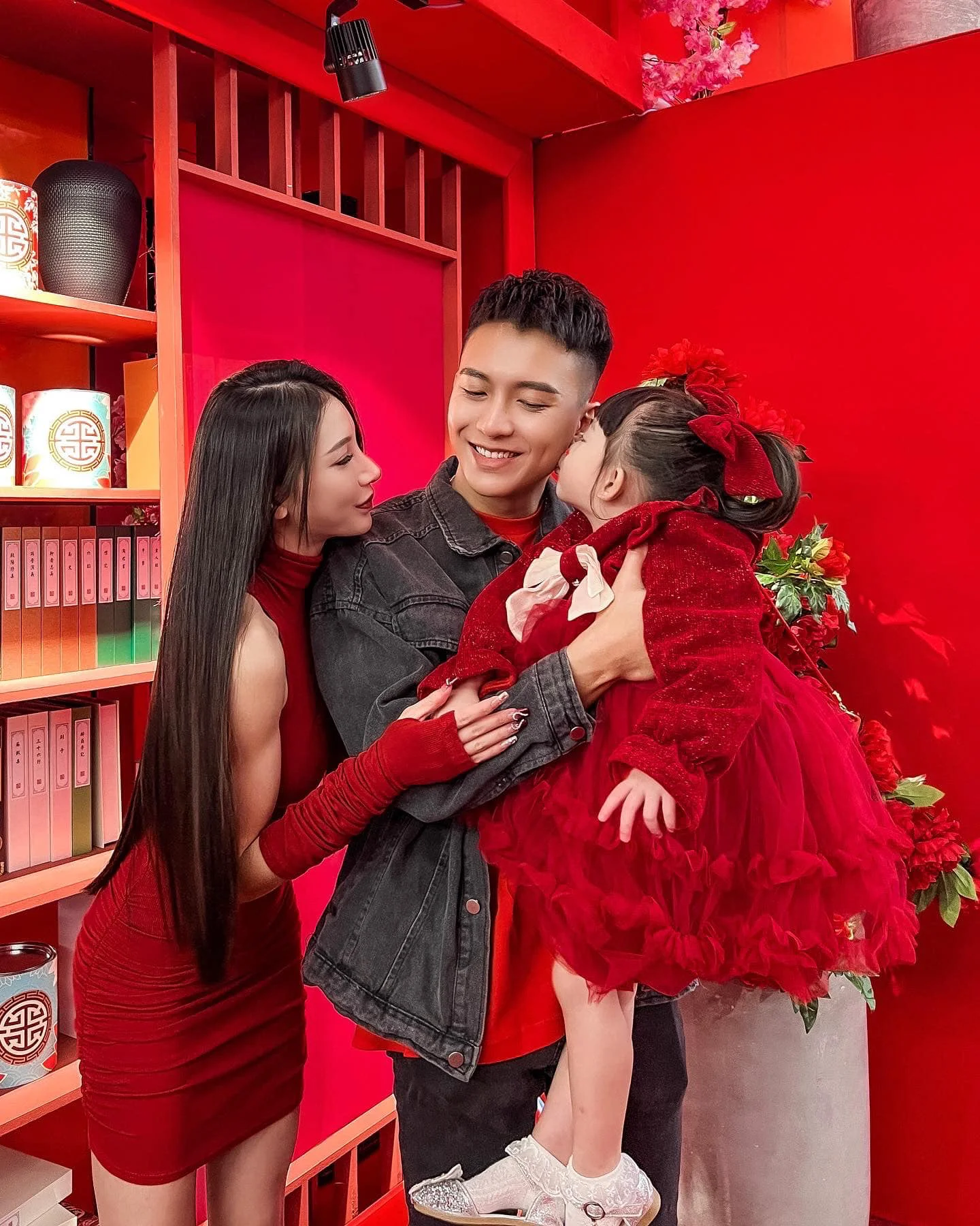 一男一女与小女孩身穿红色服饰在喜庆背景下合影，气氛温馨幸福。