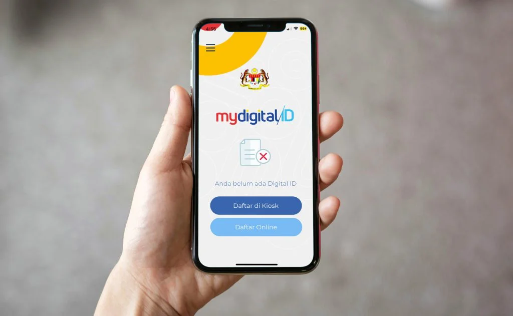 手持手机显示 MyDigital ID 登录界面显示“Daftar di Kiosk”和“Daftar Online”按钮。