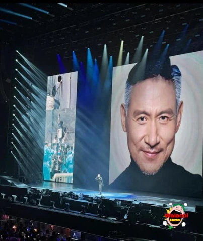 张学友独自站在舞台中央，大屏幕投影温暖笑容画面